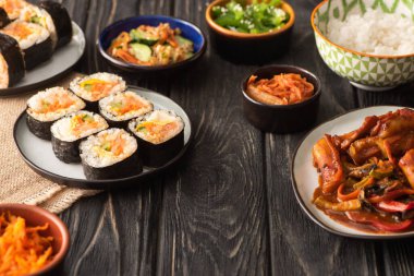 Tahta yüzeydeki lezzetli Kore yemeklerinin yanında geleneksel gimbap seçici odak noktası 