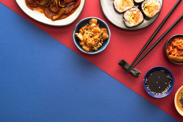 top view of bowls and plates with korean kimchi and kimbap on blue and crimson  