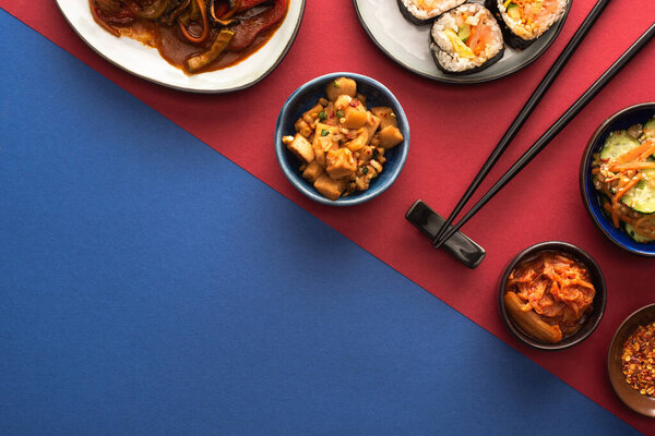 top view of bowls and plates with spicy korean kimchi and kimbap on blue and crimson  