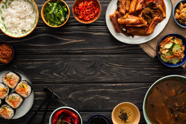 top view of korean traditional and spicy dishes near chopsticks and cotton napkin on wooden surface 