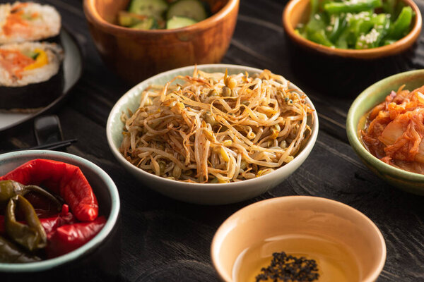 selective focus of mung beans near pickled chili peppers, sesame in oil and side dishes on wooden surface