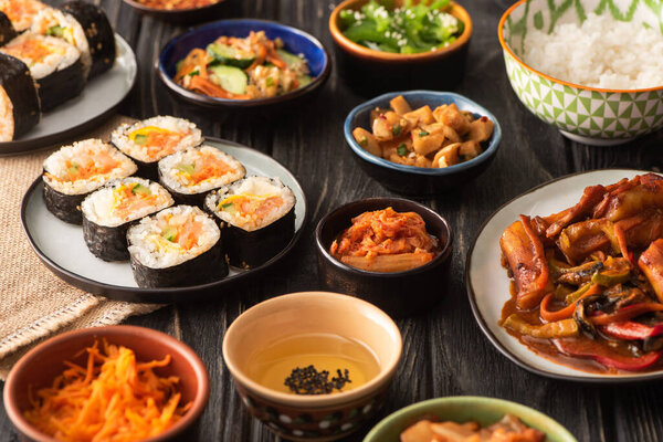 selective focus of traditional gimbap and kimchi near tasty korean dishes on wooden surface 