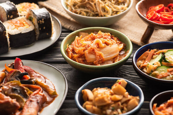 selective focus of traditional spicy kimchi and topokki near tasty korean dishes on wooden surface 