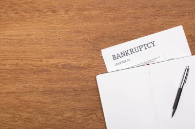 top view of bankruptcy paper and blank notebook with pen on wooden background clipart