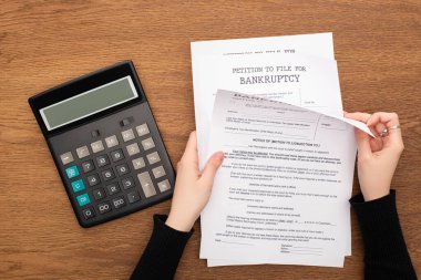 cropped view of woman with bankruptcy papers near calculator on wooden background clipart