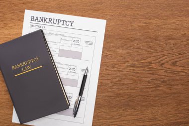 top view of bankruptcy paper, law book and pen on wooden background clipart