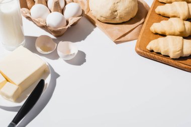 Tahta üzerinde taze kruvasanlar ham hamur, süt, tereyağı ve beyaz arka planda yumurtalar.