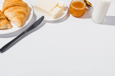 tasty fresh baked croissants on plate near glass of milk, butter with knife and jam on white background clipart