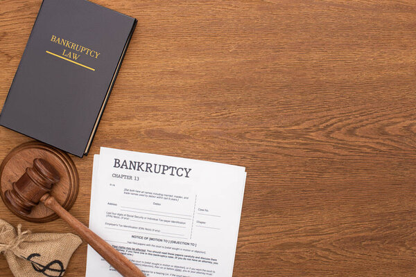 top view of bankruptcy law book, documents, money bag and gavel on wooden background