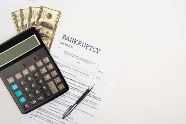 top view of bankruptcy paper with pen, money and calculator on white background
