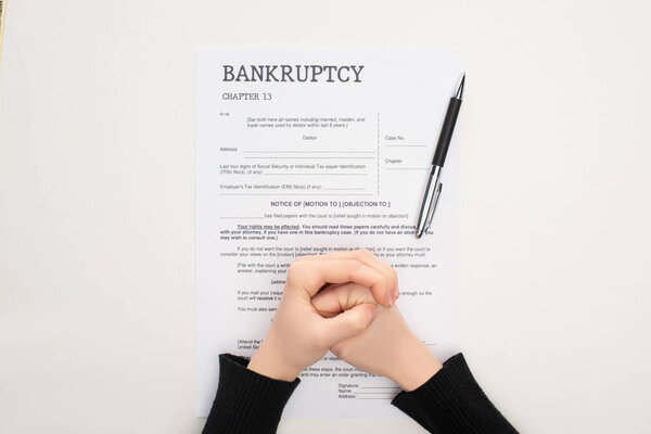 обрезанный вид женских сжатых рук на бумаге для банкротства рядом с ручкой на белом фоне
 