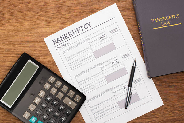 обзор бумаги о банкротстве, книги законов и калькулятора на деревянном фоне
