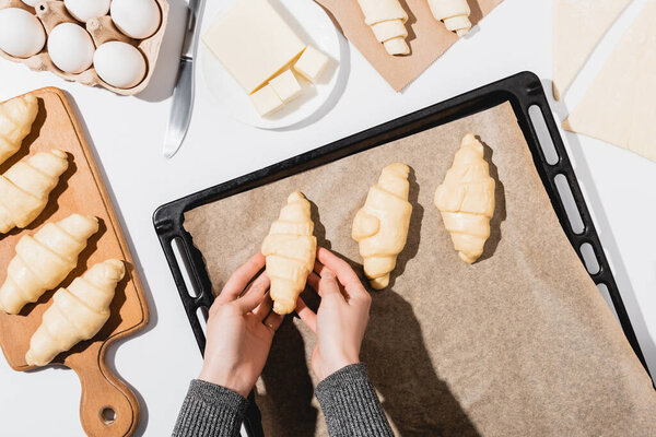 обрезанный вид женщины положить круассаны на поднос для выпечки на белом фоне

