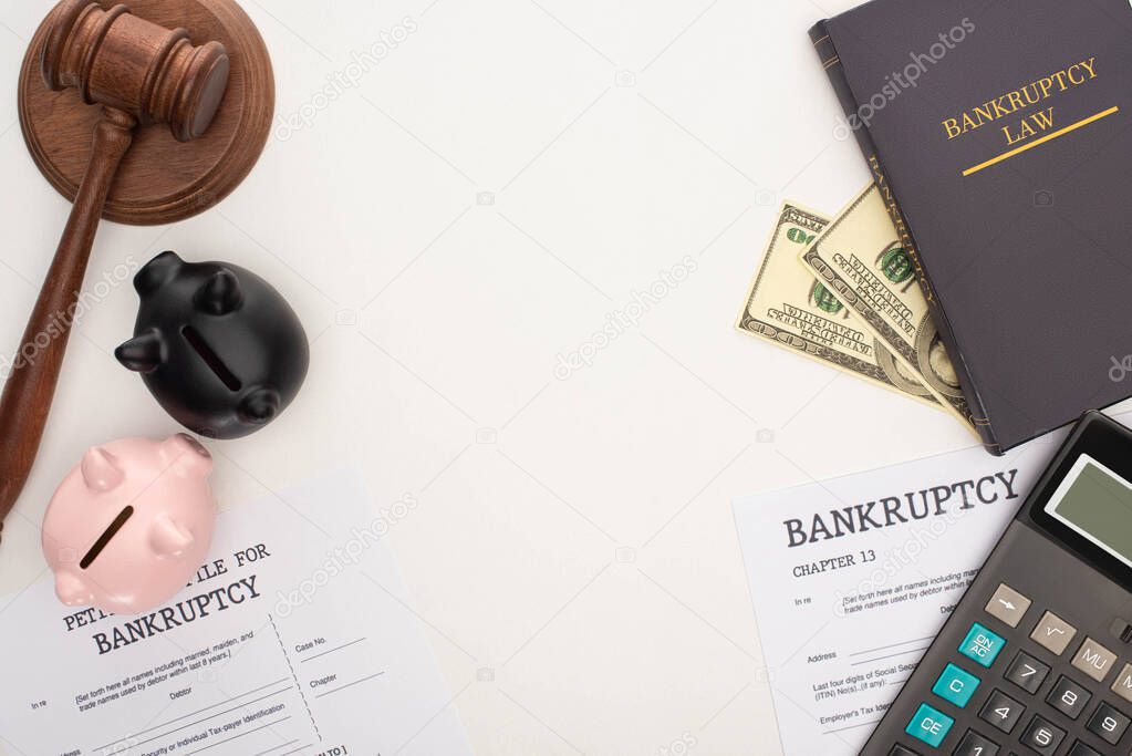 top view of bankruptcy papers and law book, gavel, piggy banks, money and calculator on white background