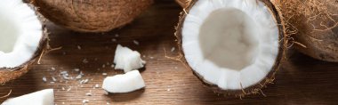 fresh tasty whole and cracked coconuts and flakes on wooden table, panoramic shot clipart