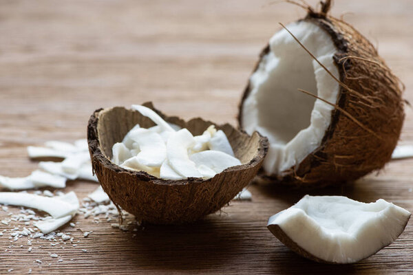 selective focus of fresh tasty coconut half near flakes in shell on wooden table