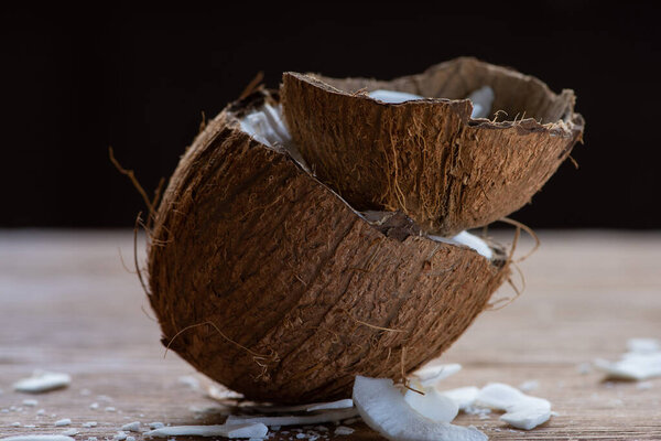 selective focus of fresh tasty coconut half and flakes in shell on wooden table isolated on black