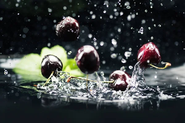 Ripe cherries falling in water — Stock Photo