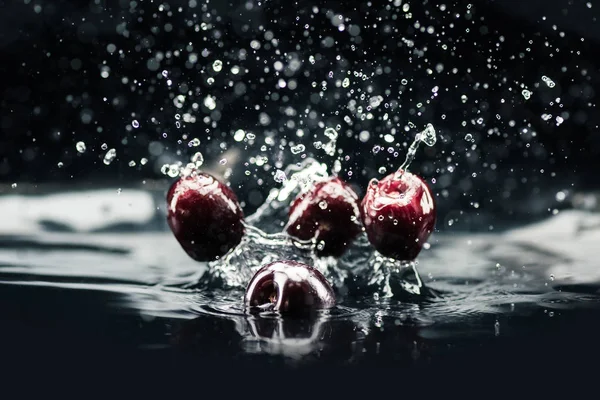 Ripe cherries falling in water — Stock Photo