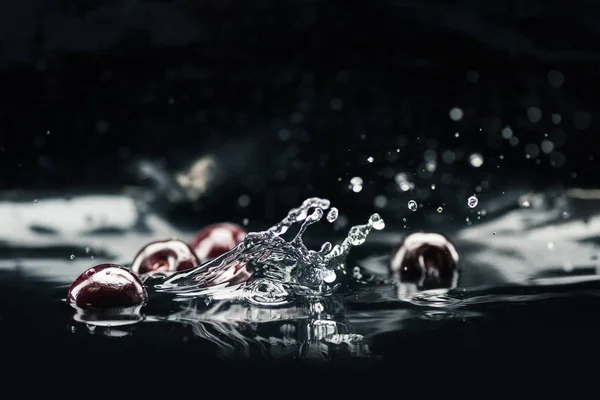 Ripe cherries falling in water — Stock Photo