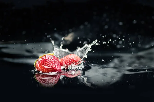 Fresas maduras que caen en el agua - foto de stock