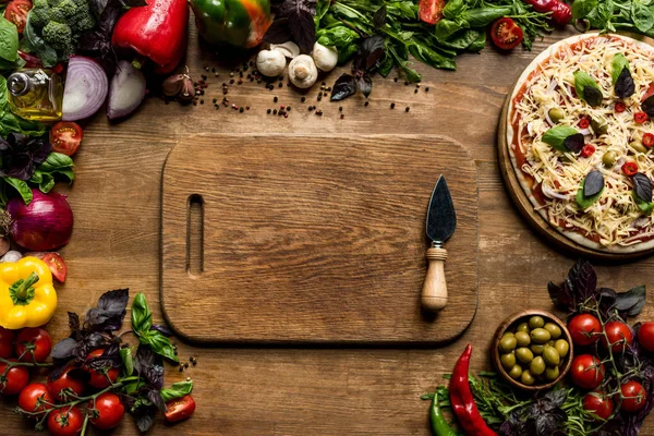 Cutting board, pizza and ingredients — Stock Photo