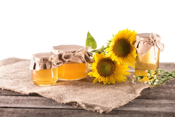 Sunflowers and honey in glass jars — Stock Photo