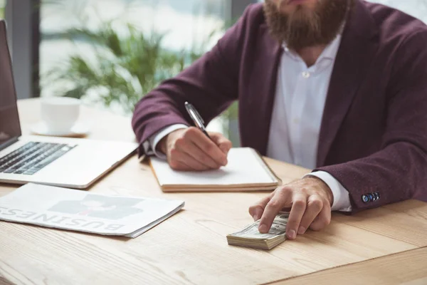 Hombre de negocios escribiendo y sosteniendo dólar - foto de stock