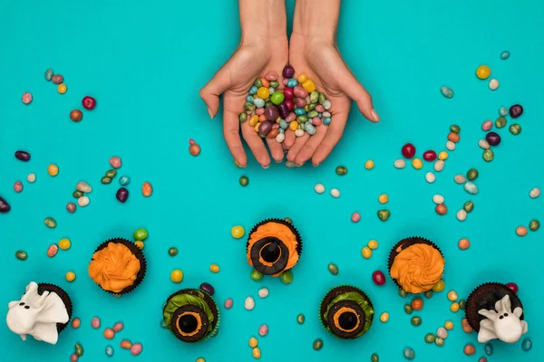 Hands with candies and halloween cupcakes — Stock Photo