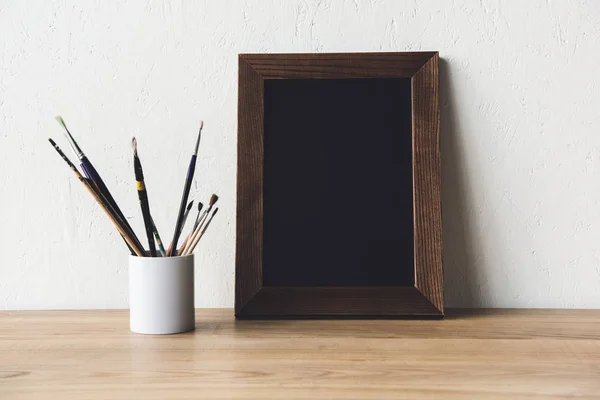 Photo frame and paintbrushes on tabletop — Stock Photo