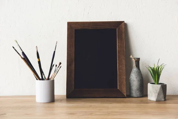 Photo frame and paintbrushes on tabletop — Stock Photo