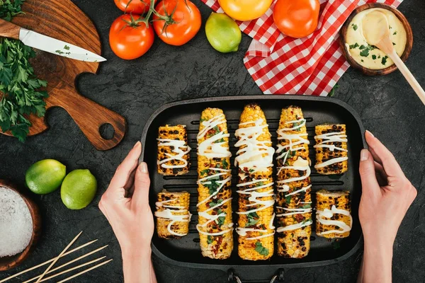 Woman holding baking tray with corncobs — Stock Photo