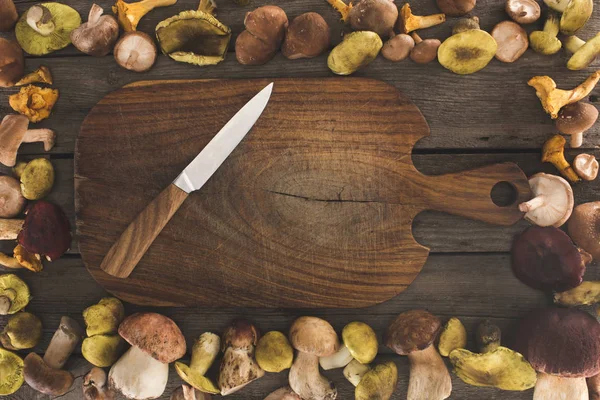 Cutting board with knife and mushrooms around — Stock Photo