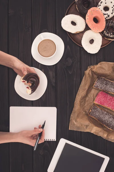 Person eating donut and taking notes — Stock Photo