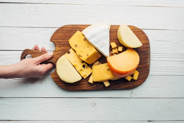 Mano y queso surtido sobre tabla de madera - foto de stock