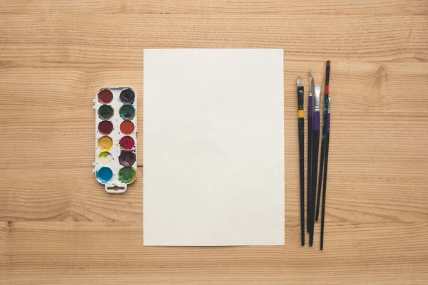 Sheet of paper with paints and brushes — Stock Photo