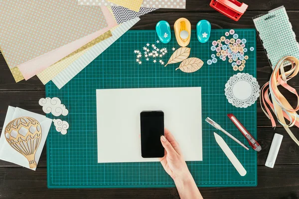 Imagen recortada de la mujer sosteniendo el teléfono inteligente sobre una hoja de papel vacía - foto de stock