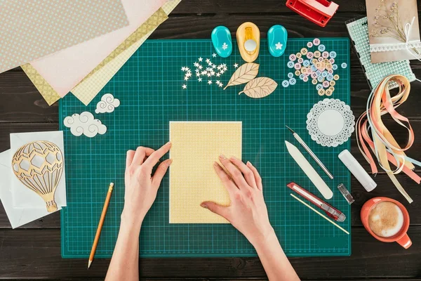 Cropped image of designer sitting at working table with template for scrapbooking postcard — Stock Photo