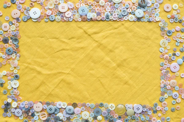 Vista superior del marco de botones de colores sobre fondo de tela amarilla con espacio de copia - foto de stock