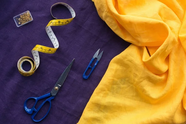 Вид зверху на ножиці, вимірювальна стрічка і коробка з шпильками над фіолетовою тканиною — стокове фото