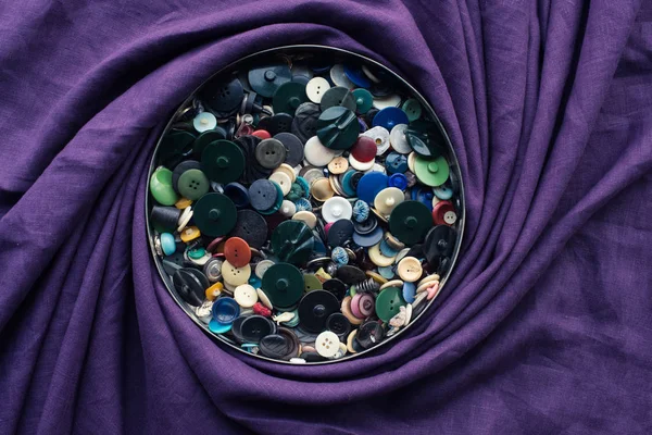 Lot of buttons in circle box, covered by purple fabric — Stock Photo