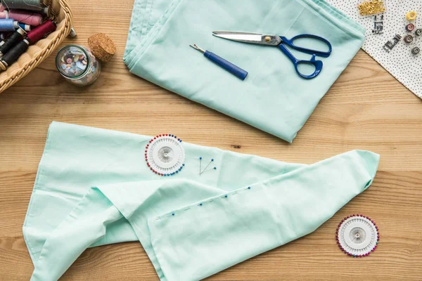 Vista dall'alto del posto di lavoro della sarta sul tavolo con tessuto, forbici, aghi, nastro di misurazione e bottoni — Foto stock