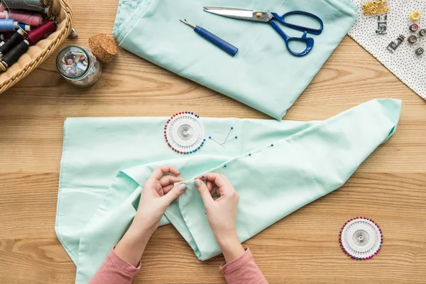 Vue du dessus du tissu de couture des mains féminines recadrées avec aiguille sur le lieu de travail de couturière — Photo de stock