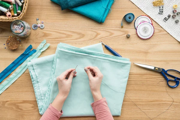 Vue du dessus du tissu de couture des mains féminines recadrées avec aiguille sur le lieu de travail de couturière — Photo de stock