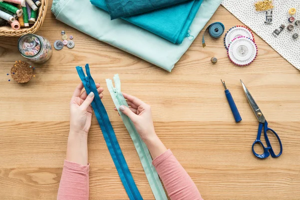 Vista superior das mãos femininas cortadas segurando armários zip no local de trabalho de costureira — Fotografia de Stock