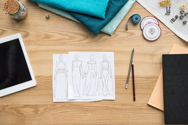 Top view of seamstress workplace on table with fabric, tablet and sketches — Stock Photo