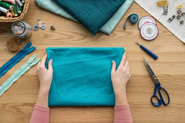 Vue du dessus du tissu pliant des mains féminines coupées sur le lieu de travail de couturière — Photo de stock