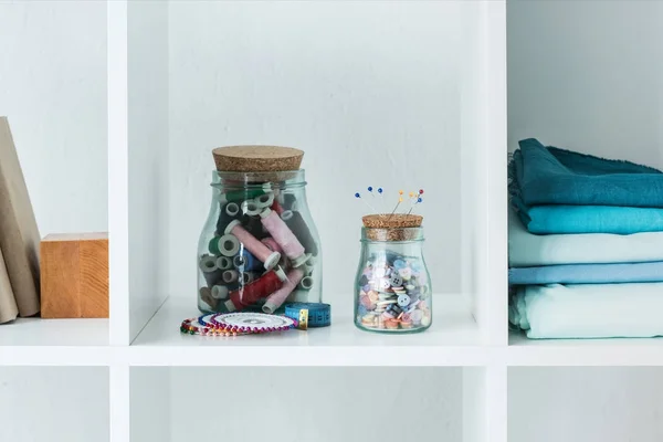 Pile of folded colored fabric with stitchings in bottles on white shelf — Stock Photo