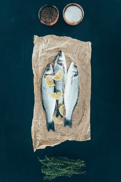 Vista superior de pescado orgánico saludable con rodajas de limón sobre papel de hornear sobre negro - foto de stock