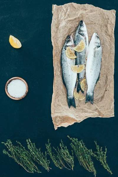 Vista superior de peixe são com partes de limão no papel no preto — Fotografia de Stock